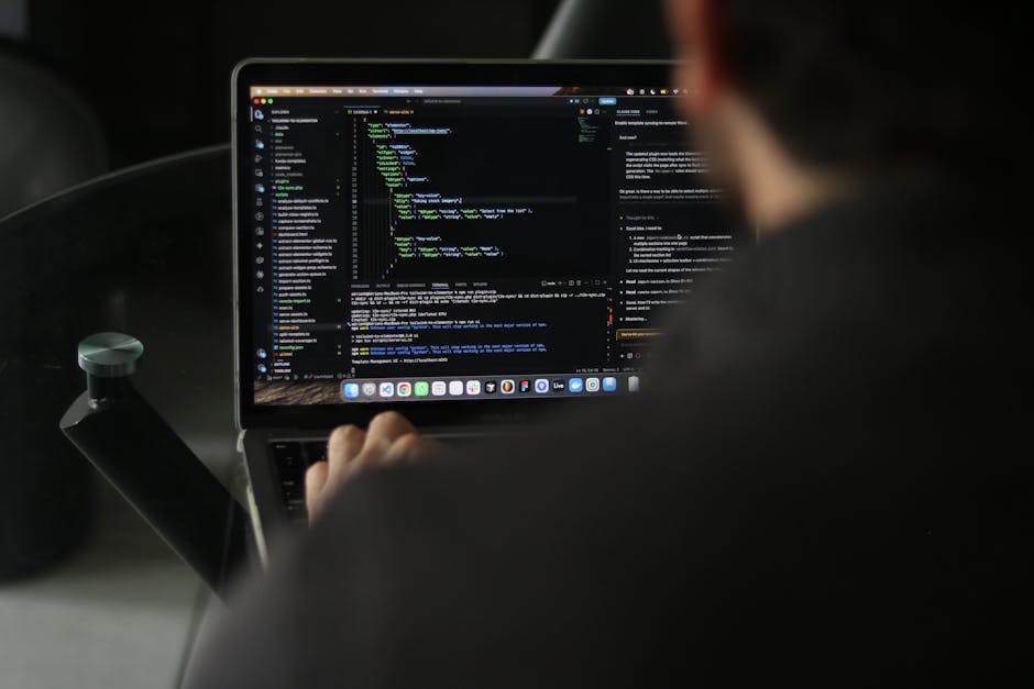 A close-up of a person's hands working on a laptop with a dark screen displaying lines of colorful code, placed on a black reflective surface. The background is blurred, showing a cozy indoor setting 